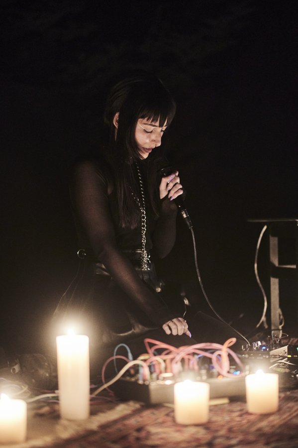 Lindred performing live with microphone and modular synth surrounded by candles
