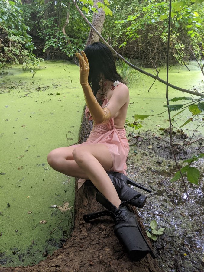 Lindred in pink dress and platform boots beside a green pond