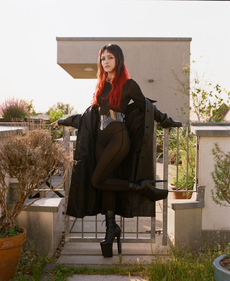 Lindred standing on rooftop in black coat with red and black hair