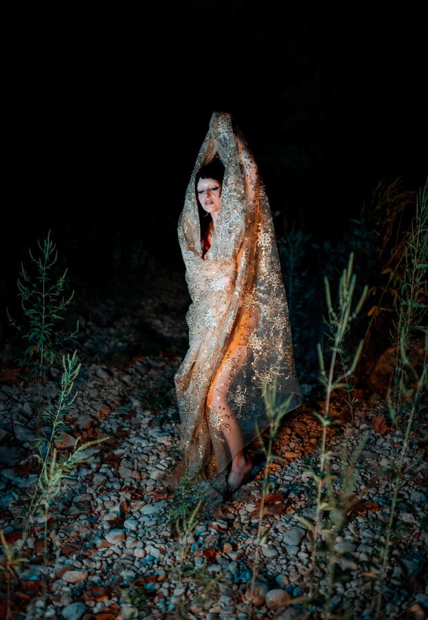 Lindred draped in sequined gold fabric outdoors at night